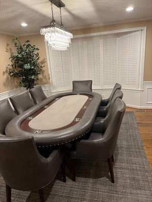 Luxury oval poker table with grey leather rail, beige cloth and steel cupholders in a dining room