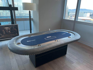 Luxury oval poker table with navy cloth, grey leather rail and a solid box base in a city apartment