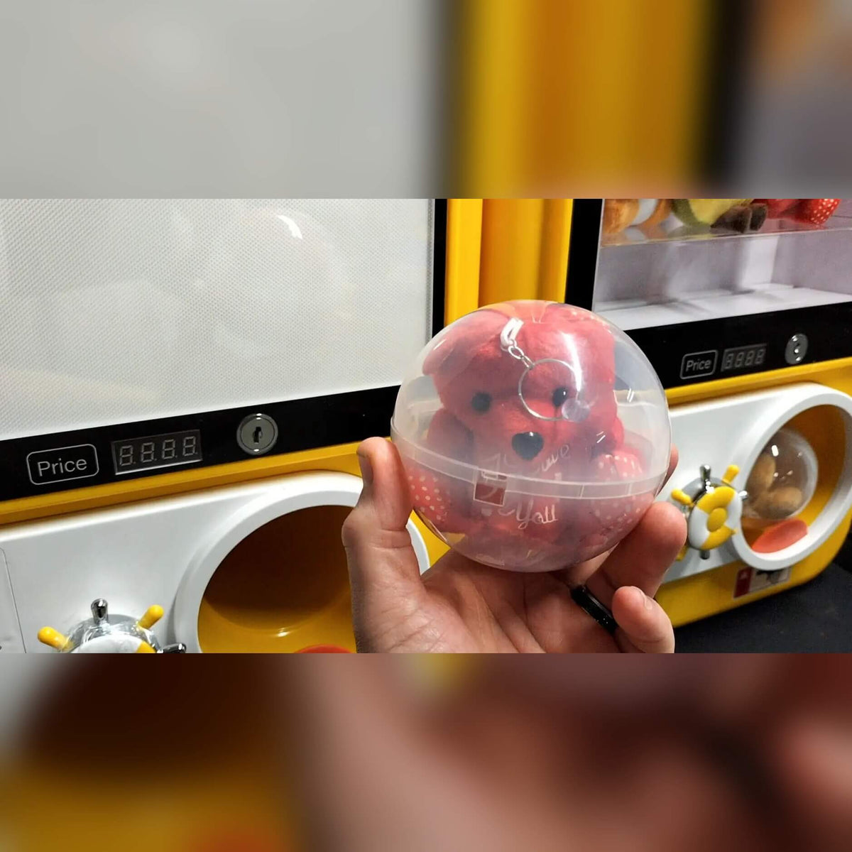 A hand holding a pink capsule from the capsule vending machine