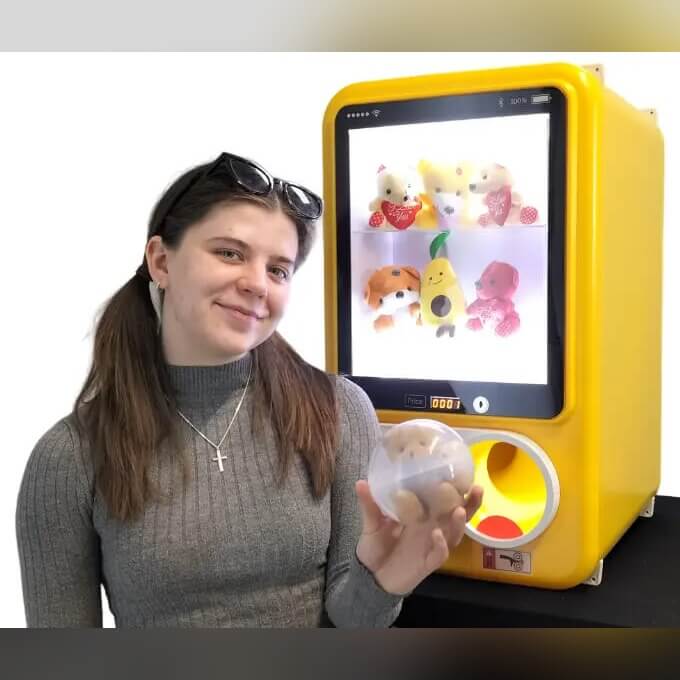 A woman holding a capsule from a yellow MadeForArcade capsule vending machine