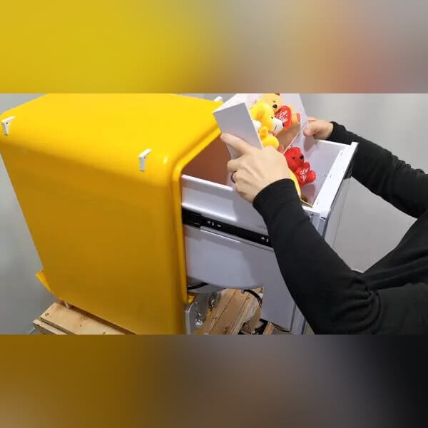 A hand turning the knob on a yellow capsule vending machine