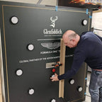 Man installing a custom MadeForArcade batak reflex wall branded for Glenfiddich and the Aston Martin Formula One team
