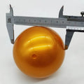 Solid gold-colour 100mm capsule ball being measured with callipers