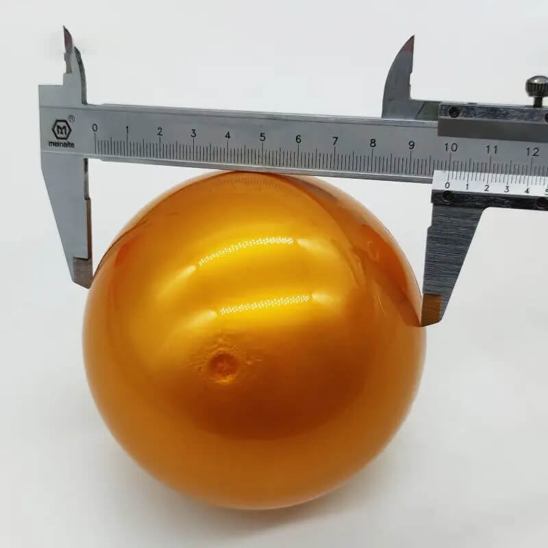 Solid gold-colour 100mm capsule ball being measured with callipers