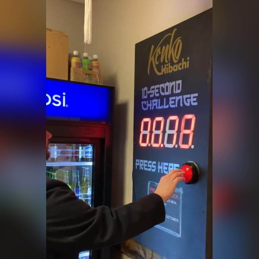 A hand pressing the button on a wall-mounted Stop the Clock game