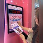A woman playing a wall-mounted Stop the Clock game on a pink stand