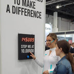 Two women playing a wall-mounted Stop the Clock game at a trade show