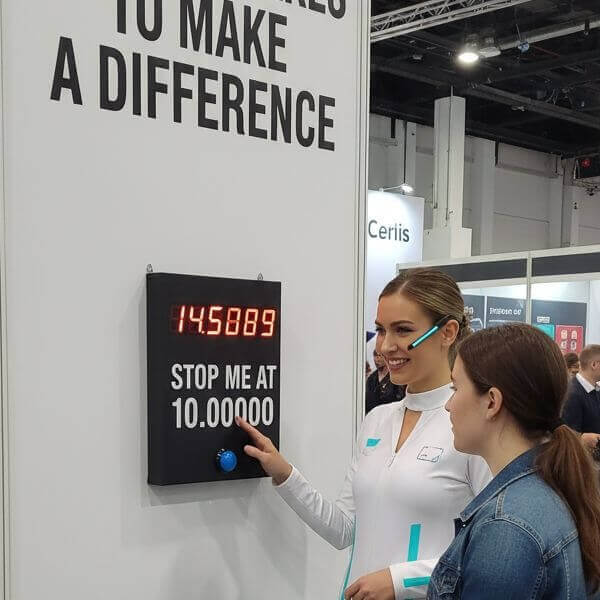 Two women playing a wall-mounted Stop the Clock game at a trade show