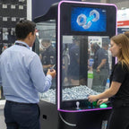 Visitors at a black video screen claw machine at a trade show