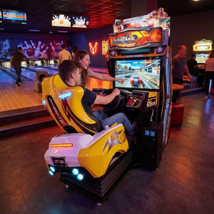 Young adult racing on Overtake DX at a bowling alley in the evening while a friend watches