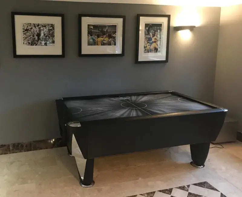 SAM Black Ice II air hockey table in a home with framed pictures on the wall