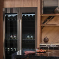 Two Signature Kitchen Suite integrated wine fridges side by side in a wood-panelled kitchen with wine glasses on the counter
