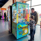 Boy playing the WIK Candy House claw machine while his dad watches in a seaside amusement arcade