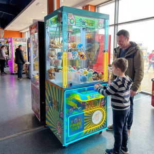 Boy playing the WIK Candy House claw machine while his dad watches in a seaside amusement arcade