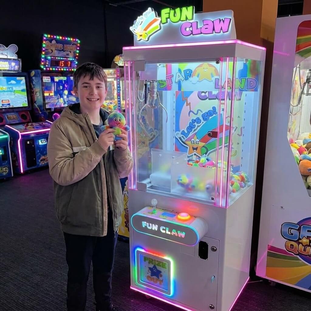 Smiling teenager holding a small plush toy won from the WIK Fun Claw in a family entertainment centre