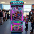 Boy playing the WIK Super Clip prize machine while his dad watches in a seaside amusement arcade