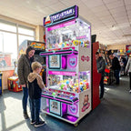 Boy playing the WIK Toy Star Mini 4 player claw machine while his mum watches in a seaside amusement arcade