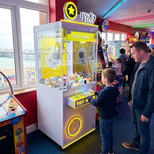 Boy playing the WIK Toy Star Small claw machine while his dad watches in a seaside amusement arcade