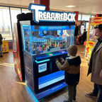 Child pressing the buttons on the WIK Treasure Box Clip prize machine while his dad watches in a seaside arcade