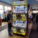Boy playing the WIK Trend Star 4 player claw machine while his dad watches in a seaside amusement arcade