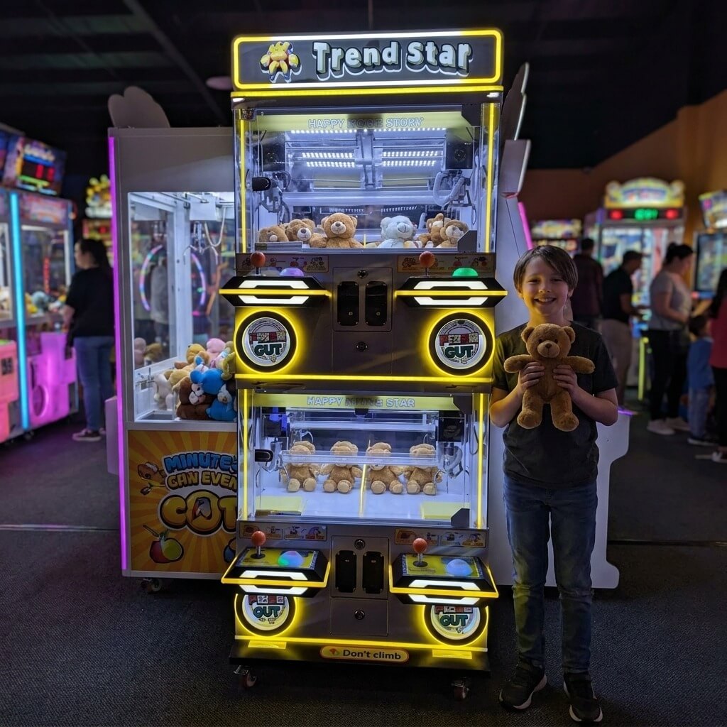 Smiling boy holding a teddy bear won from the WIK Trend Star claw machine in a family entertainment centre